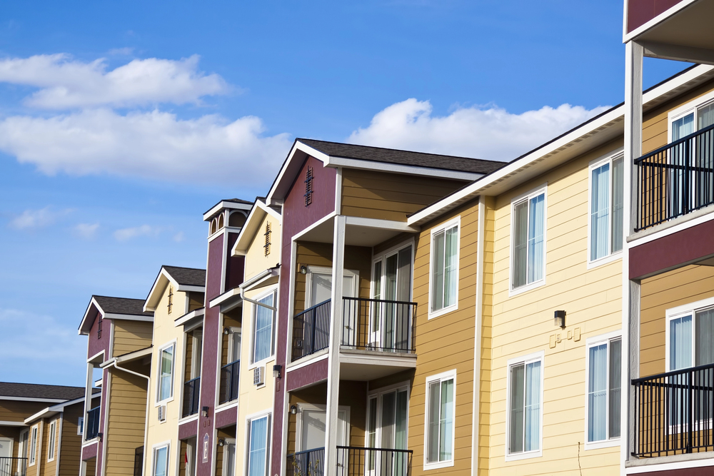 Modern apartment building with yellow and brown siding, multiple balconies, and large windows under a blue sky with scattered clouds—perfect for those seeking urban living or guidance from an experienced real estate lawyer in Victoria, BC.